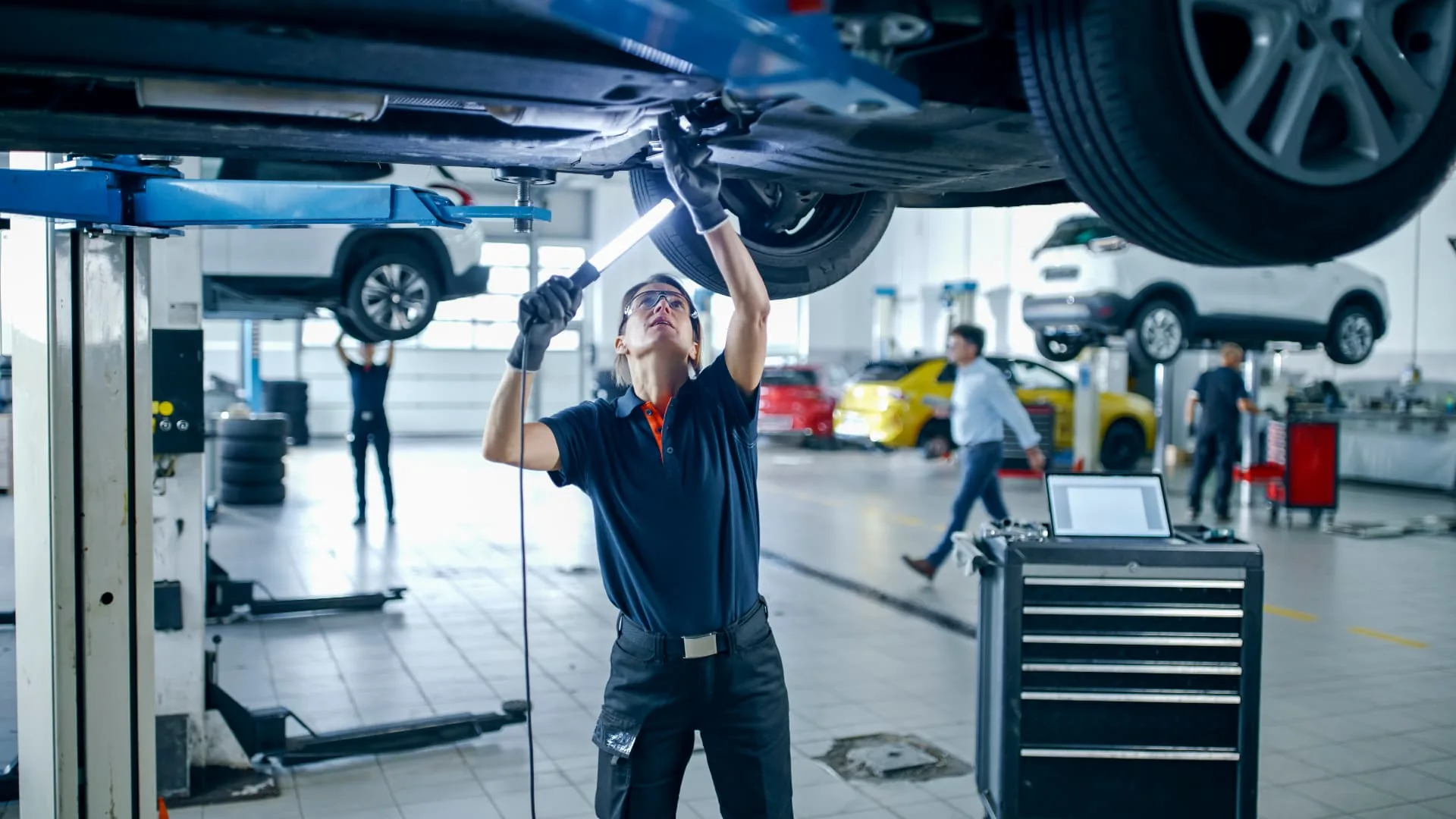 Mechanic inspecting the underside of a car raised on a workshop hoist